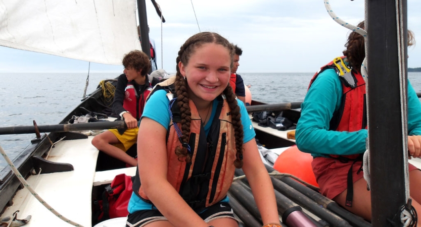 A person wearing a life jackets smiles while sitting on a sailboat. 